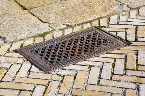 Iron rusty rectangular manhole with shaped holes in form of crosses in lid. Stock Photos