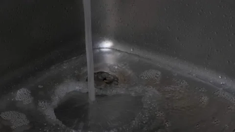 In an iron sink with a plug inserted, a stream of water begins to pour Stock Footage 150974145