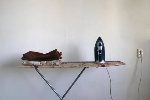 An ironing board, an iron plugged into a socket, and ironed linen Stock Photos