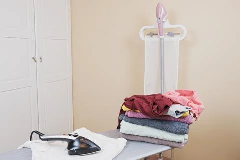 Ironing board with iron, vertical household garment steamer and a stack of cl 스톡 사진