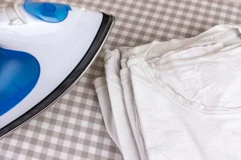 Ironing stack of white t-shirts on board. A blue iron and a pack of wrinkled Stock Photos