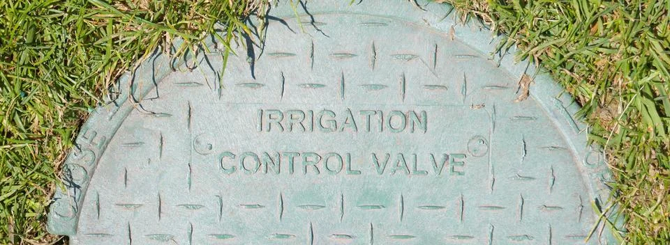 Irrigation control valve cover embedded in grassy ground Stock Photos