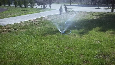 The irrigation device is installed in the city park and sprays water on the Stock Footage 201021887