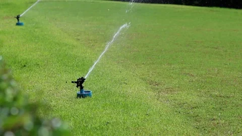 Irrigation System Spraying Water Over Growing Crop in a Field at Sunset Garden Vídeos de archivo 334657656