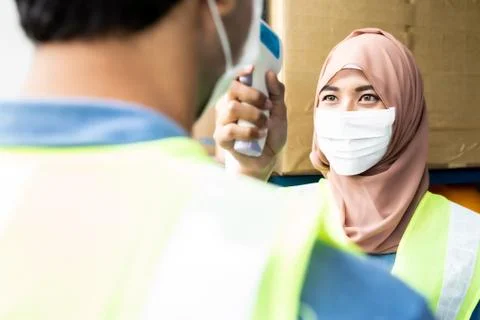 Islam Muslim asian warehouse worker take temperature to another worker Stock Photos