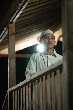 An Islamic man praying on the balcony while wearing a white Muslim dress in t Stock Photos