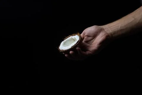 Isolated coconut on a black background. Half of a coconut in a man's hand on a d Foto stock