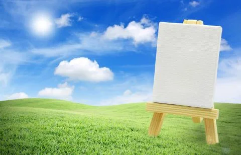 Isolated easel with empty canvas on green grass, blue sky Stock Photos