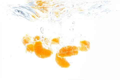 Isolated falling orange segments into water. Peeled pieces of orange fruit in Stock Photos