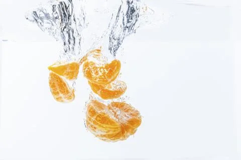 Isolated falling orange segments into water. Peeled pieces of orange fruit in 库存照片