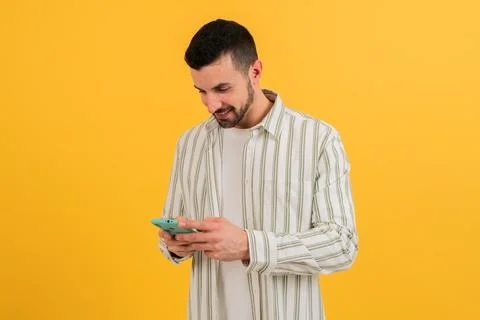 Isolated guy using his smartphone, cell phone chatting and smiling in yellow Stock Photos