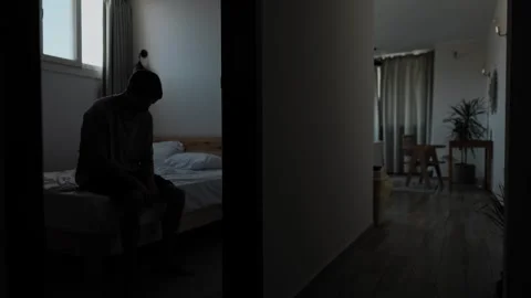 Isolated man enters empty bedroom and sits alone on bed Stock Footage 346246563