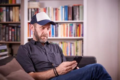 Isolated man sitting on a couch in front of bookshelf pondering Stock Photos
