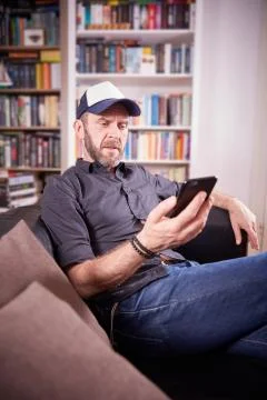 Isolated man sitting on a couch in front of bookshelf pondering Stock Photos