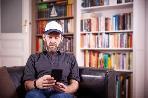 Isolated man sitting on a couch in front of bookshelf pondering Stock Photos