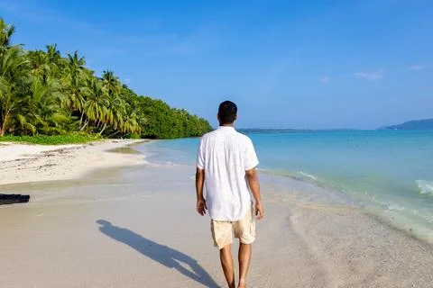 Isolated man walking at pristine white sand beach with rolling sea waves at.. Stock Photos