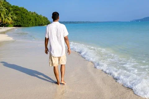 Isolated man walking at pristine white sand beach with rolling sea waves at.. Stock Photos