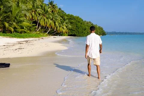 Isolated man walking at pristine white sand beach with rolling sea waves at.. Foto stock