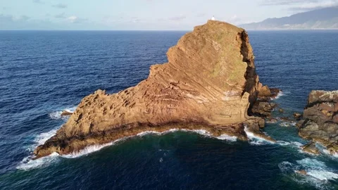 Isolated rock stack of Ilhéu Mole with folded rock layers and small lighthouse Stock Footage 311895398