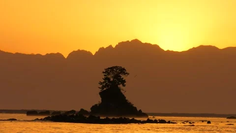 Isolated Rocky Islet with Pine Tree Silhouetted Against Golden Mountain Dawn Stock Footage 337404334
