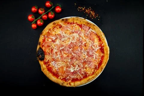 Isolated round pizza on black background with tomatoes Stock Photos