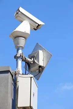 Isolated surveillance security camera or cctv on blue sky, left perspective Stock Photos