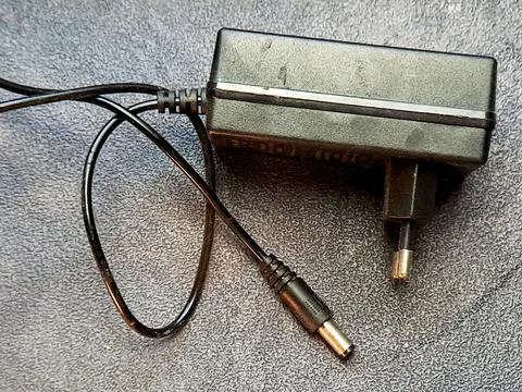 Isolated view of a black AC adapter with a power cord on a textured gray su.. Stock Photos
