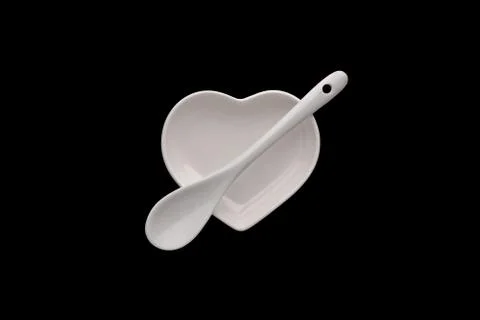 An isolated white ceramic saucer in the shape of a heart and a spoon across the Stock Photos