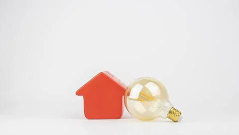 Isolated, yellow retro bulb leaning on a red house figurine Stock Photos