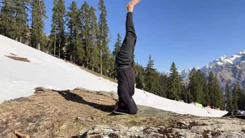 Isolated yogi balancing in headstand pose on hillside with pine forest and .. Stock Footage 333701095