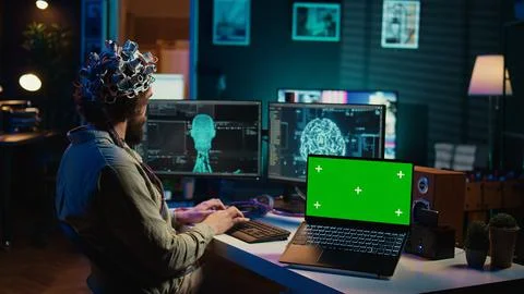 IT admin coding and using EEG headset to upload brain into green screen laptop Stock Photos