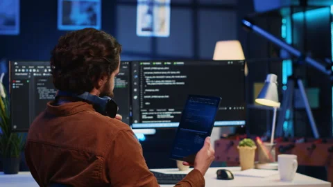 IT admin holding table, using it as reference while coding on computer Stock Footage 265338291