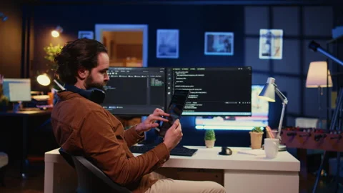 IT admin holding table, using it as reference while coding on computer Stock Footage 265511280