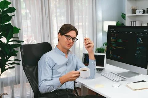 IT developer looking camera, holding coffee cup with coding on pc. Pecuniary. Stock Photos