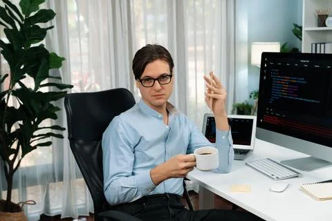 IT developer looking camera, holding coffee cup with coding on pc. Pecuniary. Stock Photos
