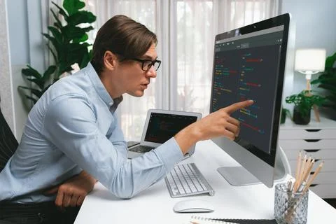 IT developer pointing on coding software on pc comparing laptop. Pecuniary. Stock Photos