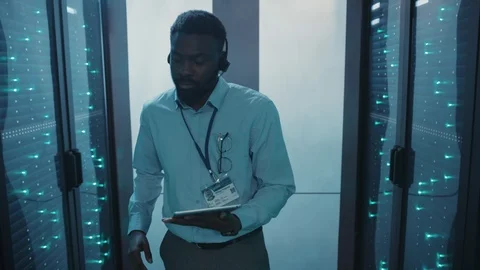 IT engineer afro-american wearing headphones examining server computers on rack Stock Footage 119081828