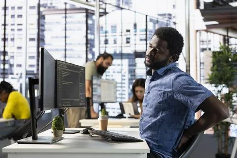 IT expert in office suffering back pain from bad posture, analyzing data Stock Photos