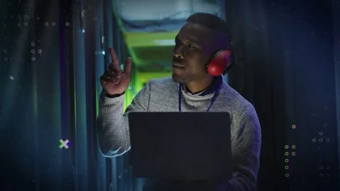 IT pro after listening with red headphones, with laptop at server racks, Stock Footage 332613816