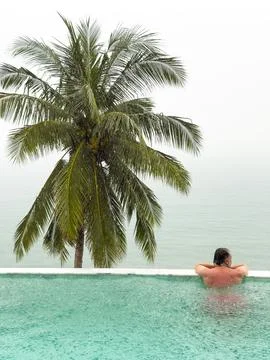 It is raining heavily in the background, a man in the pool is relaxing and Stock Photos