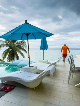 It is raining heavily in the background, a man near the pool is relaxing and Stock Photos