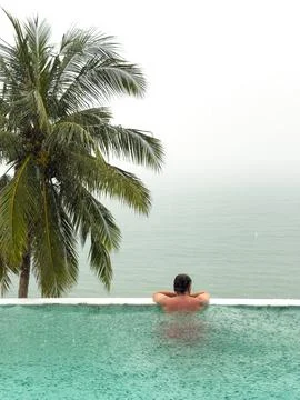 It is raining heavily in the background, a man in the pool is relaxing and Stock Photos