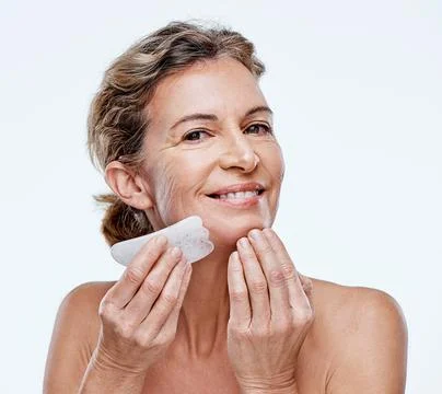 It really works. Cropped shot of a mature woman using a Qua Sha on her face. Stock Photos