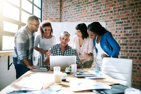 It simplifies the way we do business. a group of colleagues using a laptop Stock Photos