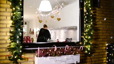 It snows outside kitchen window where woman is cooking christmas dinner Stock Footage 99724747