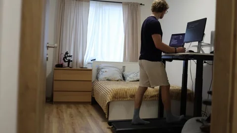 IT specialist studies technical diagrams while walking on treadmill at home Stock Footage 347269828