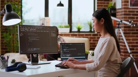 IT specialist types code on dual monitors in a cozy home office Stock Footage 319713975