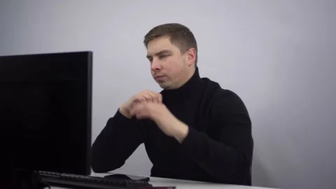 An IT specialist works at a computer and looks thoughtfully at a PC monitor. A Stock Footage 230708086