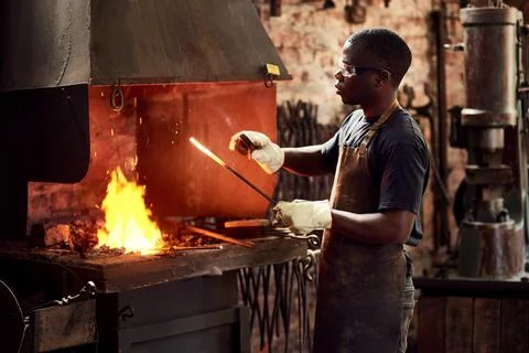 It starts glowing when it gets hot. a handsome young metal worker sharpening a 스톡 사진