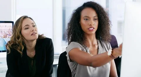 It takes two to solve this problem. two young businesswomen using a computer Stock Photos
